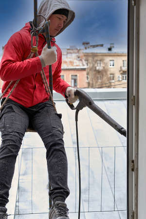 A window washer in climbing gear hangs in the window openingの写真素材
