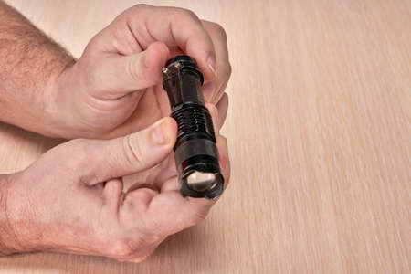 Hands hold a small black flashlight and replace the battery in itの写真素材