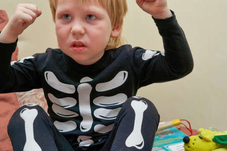 A child in a skeleton costume sits on the couch with an emotion on his faceの写真素材