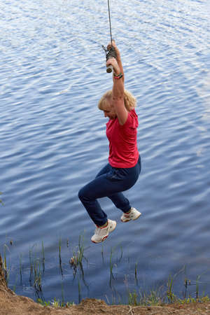 Middle aged woman in sportswear hanging on a stick with a rope above the waterの写真素材