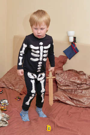 A child in a skeleton costume with a wooden sword plays on the couchの写真素材