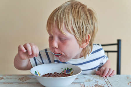 Little boy is having breakfast with chocolate balls with milkの写真素材