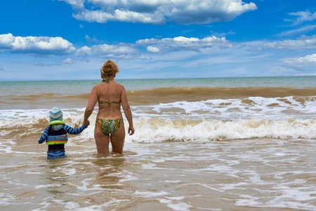 A woman and a child walk into the sea holding hands, view from the backの写真素材