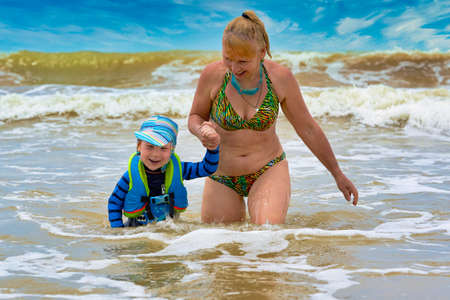 A woman takes a child in a life jacket out of the stormy seaの写真素材