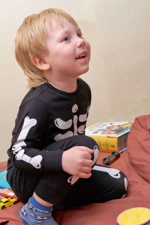A child in a skeleton costume sits on the couch with an emotion on his faceの写真素材