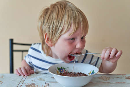 Little boy is having breakfast with chocolate balls with milkの写真素材
