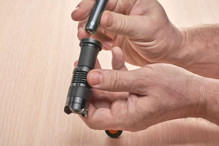 Hands hold a small black flashlight and replace the battery in itの写真素材