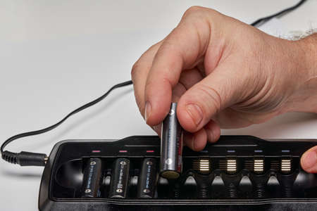 Hands insert AA batteries into black long chargerの写真素材