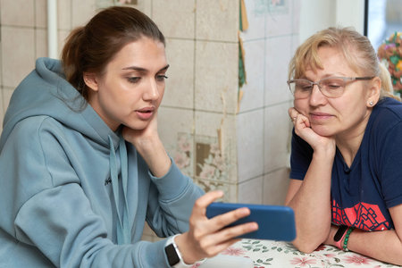 The girl shows her mother photos on the smartphone while sitting at the table
