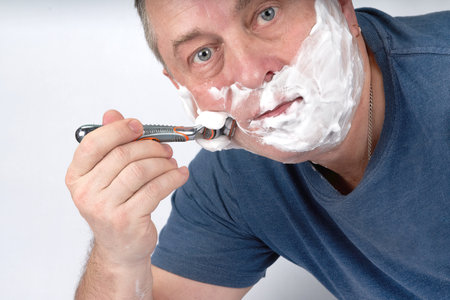 A mans face in shaving foam shaves with a safety razorの写真素材