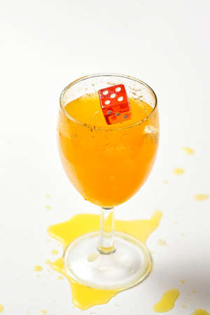A dice falling into a glass of orange liquid caused a splashの写真素材