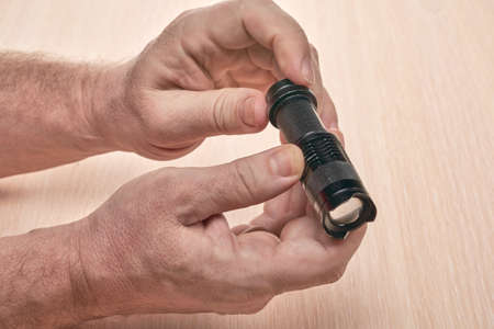 Hands hold a small black flashlight to replace the used batteryの写真素材