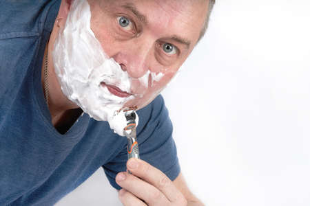A man face in shaving foam shaves with a safety razorの写真素材