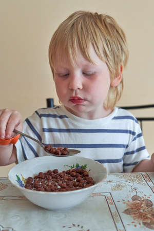 Little boy is having breakfast with chocolate balls with milkの写真素材