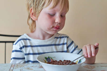 Little boy is having breakfast with chocolate balls with milkの写真素材