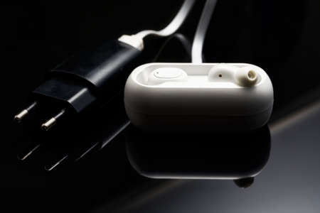 White wireless headphones plugged into charging station on a black backgroundの写真素材
