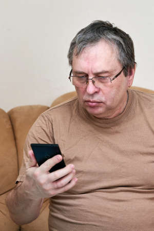 Senior citizen sitting on the couch understands the gadget, mastering smartphoneの写真素材