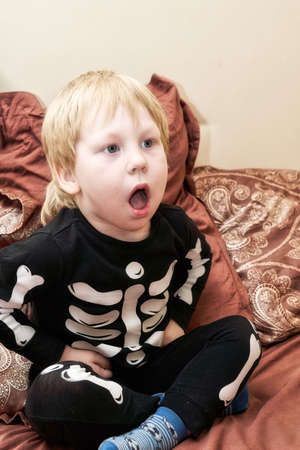 A child in a skeleton costume sits on the couch and coughs or yawnsの写真素材