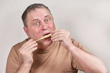 Man eating fried smelt fish holding fish with hands in front of faceの写真素材