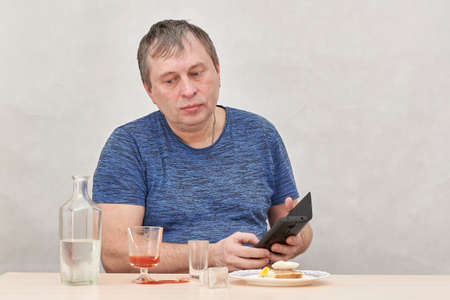 A drunkard sitting at a table dials a subscriber on the phoneの写真素材