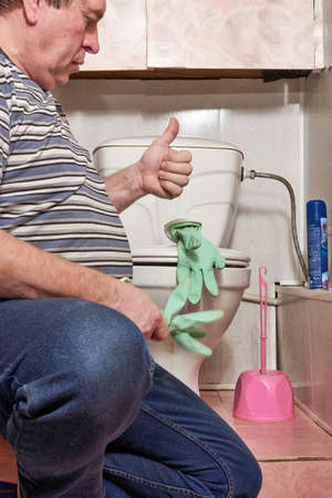 A man puts on household rubber gloves to wash a dirty toilet.の写真素材