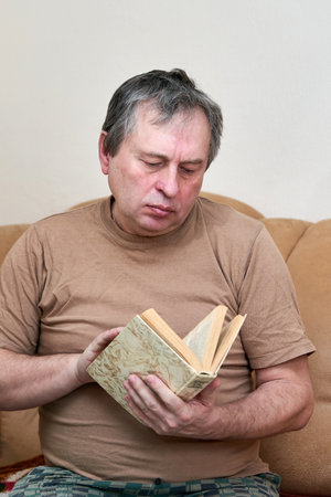 A man of age sitting on the Devani is reading a bookの写真素材