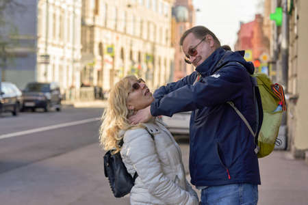 A tall man with a ponytail strangles a woman in the street with his handsの写真素材