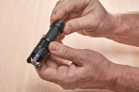 Hands hold a small black flashlight to replace the used batteryの写真素材