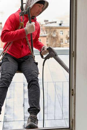 A window washer in climbing gear hangs in the window openingの写真素材