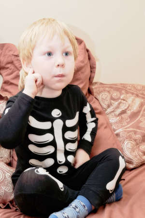 A child in a skeleton costume sits on the couch with an emotion on his faceの写真素材