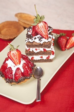 Strawberry fruit tart and chocolate strawberry cake on a plate. Both have whip cream and are beautifully decorated with chocolate shavings and strawberry halves on top.の写真素材