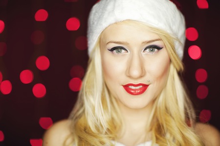 Beautiful blonde model dressed in Christmas outfit with red Christmas lights in the background.の写真素材