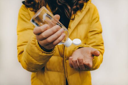 A child in a yellow jacket. In hands a bottle with gel for processing hands from germs and viruses. Antiseptic with alcohol in the composition. Horizontal photo in good quality.の写真素材