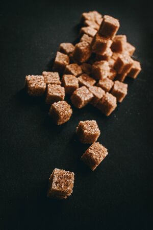 Brown cane sugar in cubes on a black background. Still life. Carbohydrates and non-diet food. Calories.の写真素材