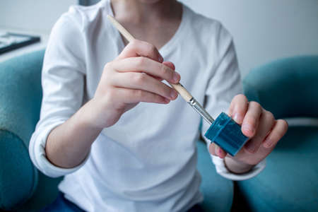 The child lowers his hand with a brush into blue paint, gouache.の写真素材