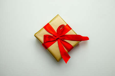 A holiday gift. Box in a gold gift wrapping with a red bow, on a white background. Merry Christmas, Happy New Year and Valentines Day greetings. Postcard. High quality photoの写真素材