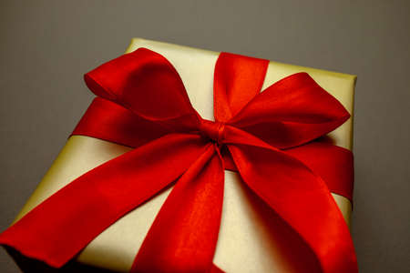 Holiday gift. Box in a gold gift wrapping with a red bow, on a red background. Merry Christmas, Happy New Year and Valentines Day greetings. Postcard. High quality photoの写真素材
