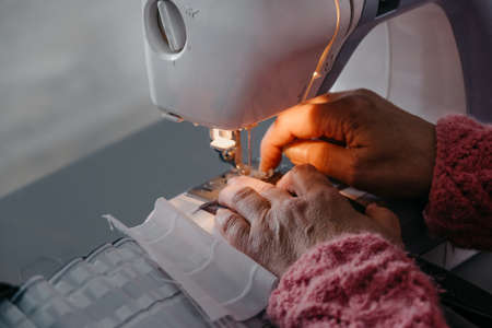 Close-up. The hands of an adult woman are sewing at a sewing machine. Manufacture of wearing apparel. High quality photoの写真素材