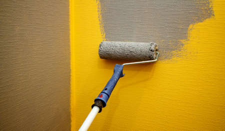 Close up roller with gray paint for painting walls. Repairs. Yellow wall. Background. Screensaver for the site. High quality photoの写真素材