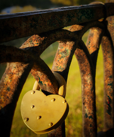 Yellow lock in form of heart hangs on old rusty fenceの写真素材