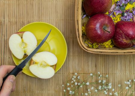 Hand holds knife after cuts apple on two parts near basket at bamboo tableclothの写真素材