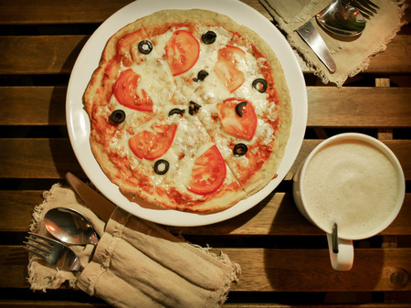 Pizza is on dish at table with cup of coffee and cutlery set, flatlayの写真素材