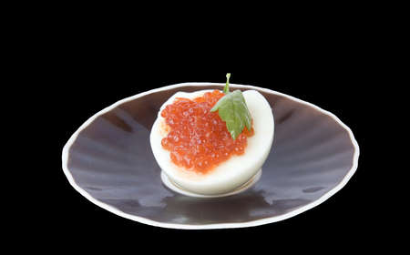 Appetizing red caviar on half egg and saucer isolated on blackの写真素材