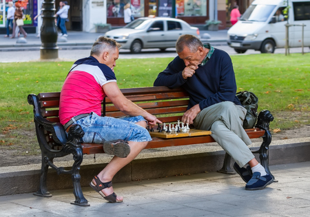 Lviv, Ukraine - 07/15/2016. Two men sitting on a bench in a park playing chess.のeditorial素材