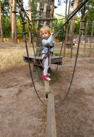 Three-year girl the blonde with a personal fall arrest system obstacle in the rope town.の写真素材