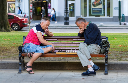 Lviv, Ukraine - July 15, 2016. Two men sitting on a bench in a park playing chess. Men play chess.のeditorial素材