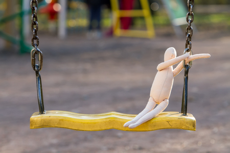 The sewn faceless doll sits on a swing and clings to the chain, in the background the playground is visible.の写真素材