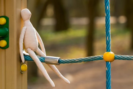 The sewn faceless doll in the profile sits on a blue rope, the construction of a playground.の写真素材