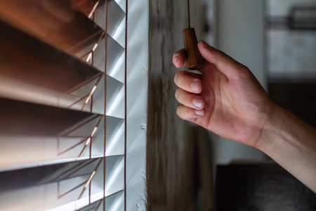 The man's right hand holds one of the control strings of the wooden shutters on the window.の写真素材