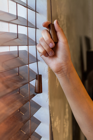 The woman's right hand holds one of the control strings of the wooden shutters on the window.の写真素材